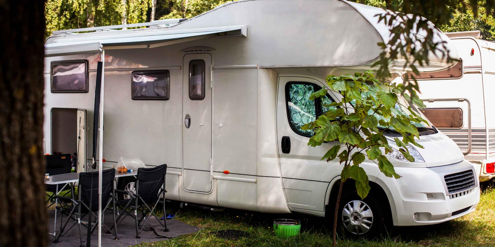 Caravane blanche avec des chaises sous des arbres