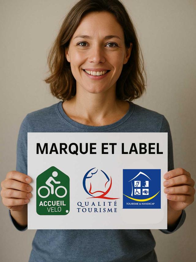 Femme tenant un panneau avec 3 logos de labels dessus: vélo accueil, marque qualité tourisme, tourisme et handicap
